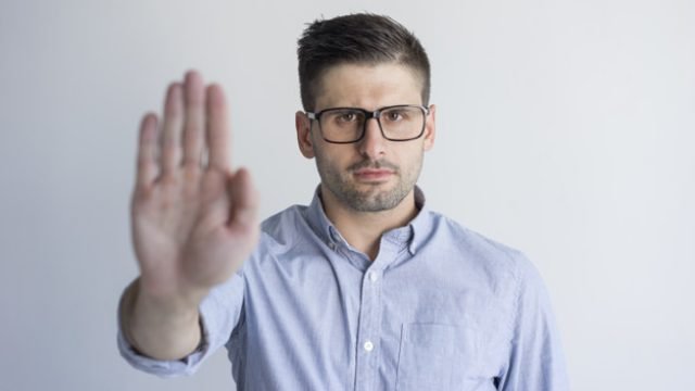 Unhappy dissatisfied young man with stubble showing rejection sign and looking at camera. Uninterested businessman making stop gesture. Refusing concept